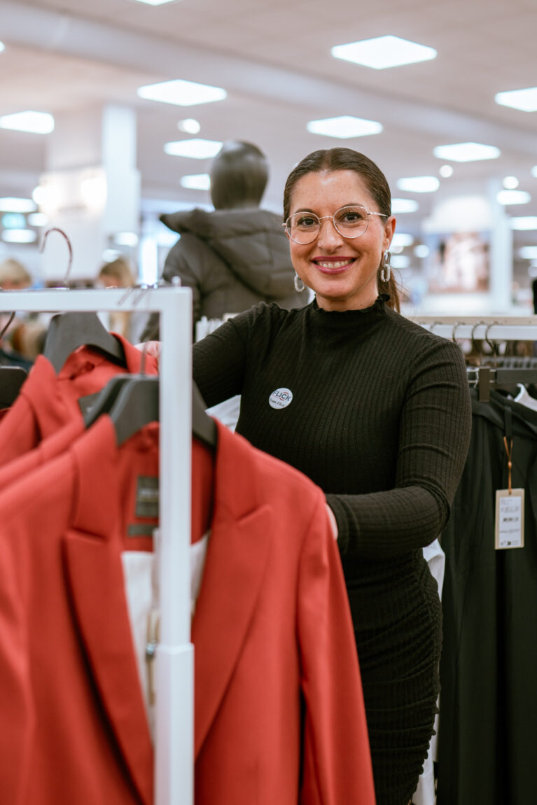 Mitarbeiterin sortiert Kleidung an einer Kleiderstange