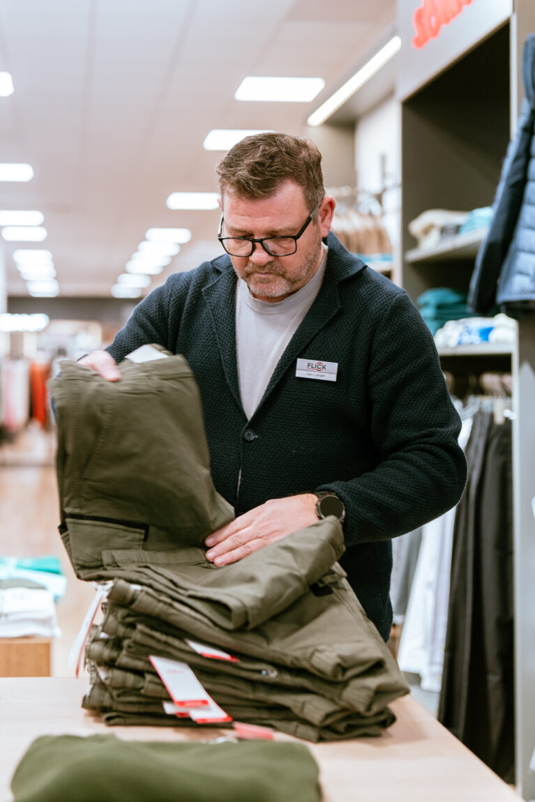 Verkäufer faltet Hose im Verkaufsbereich eines Modegeschäfts